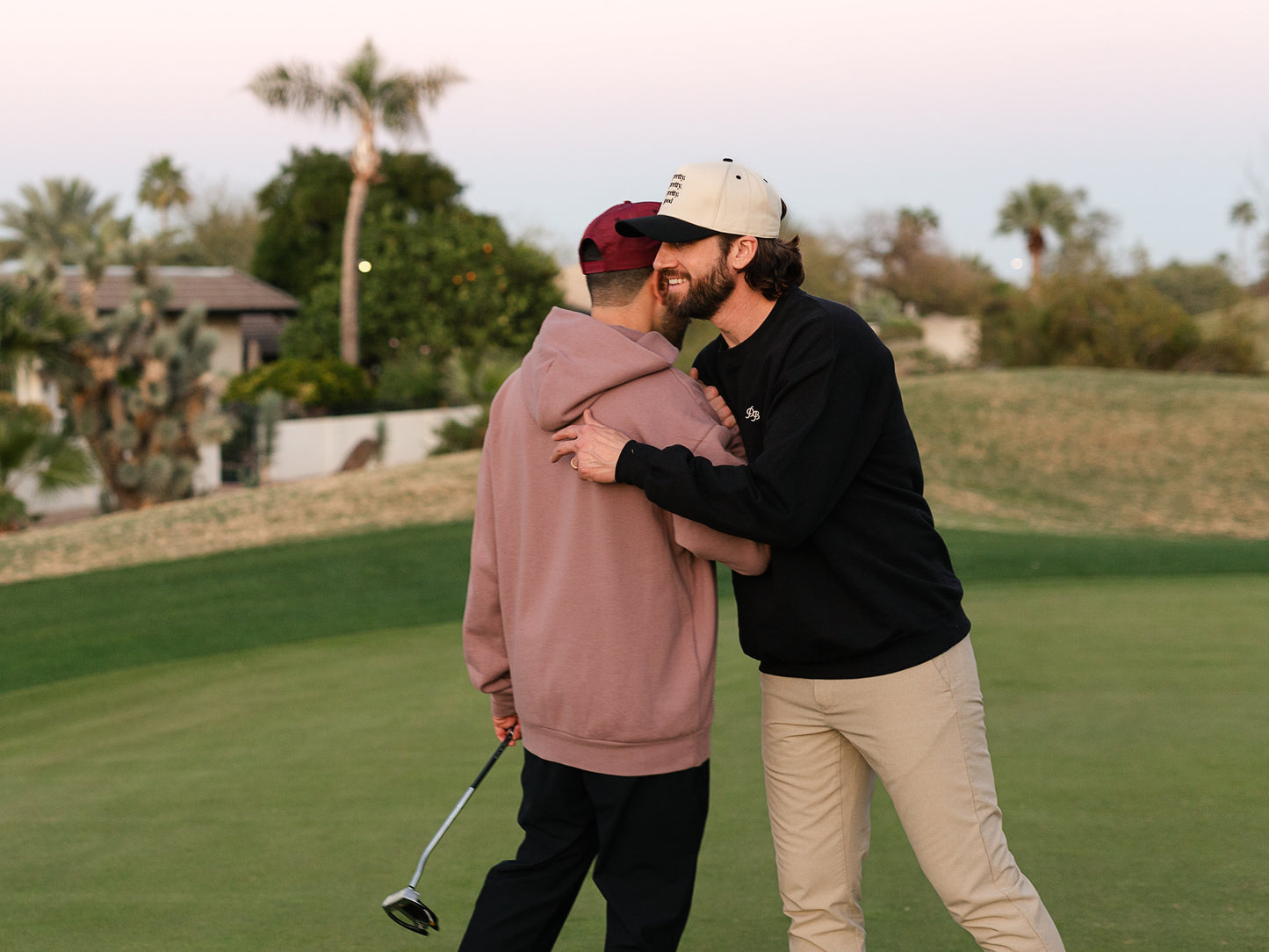 Two men embracing on a golf course with palm trees in the background