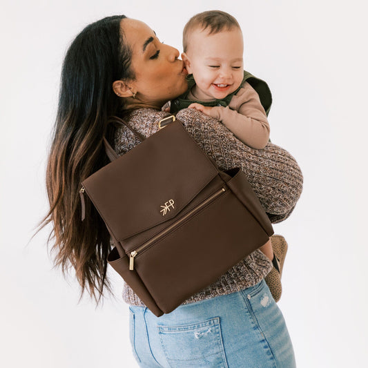Mom Holding baby with Freshly Picked Espresso Mini Classic II vegan leather mini diaper bag backpack with wipeable exterior on her shoulder