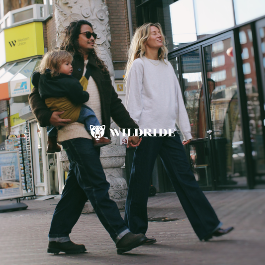 Two women walking outdoors with a child in a carrier, brand 'Wildride' visible.
