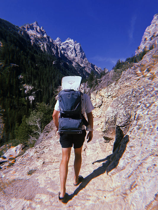 Dad hiking a rocky trail in Grand Teton National Park with a toddler in an Osprey child carrier pack