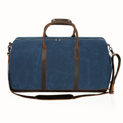 Blue duffel bag with brown leather straps and handle on a white background