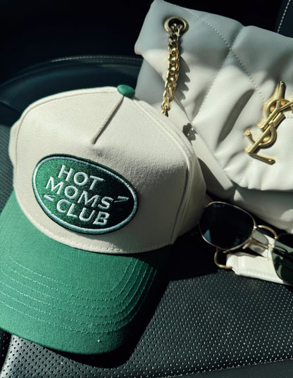 Green cap with 'Hot Moms Club' logo on a car seat next to a YSL handbag.
