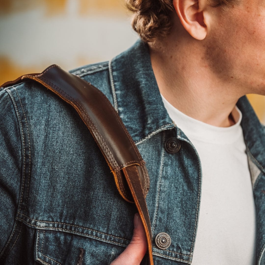Man wearing a denim jacket with a brown leather strap over shoulder