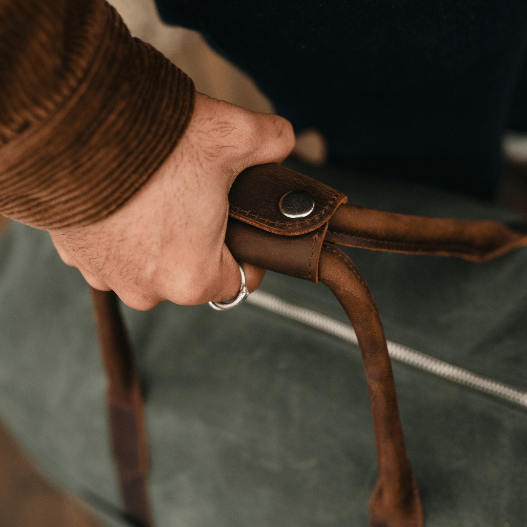 Hand holding a brown leather strap with a blurred background