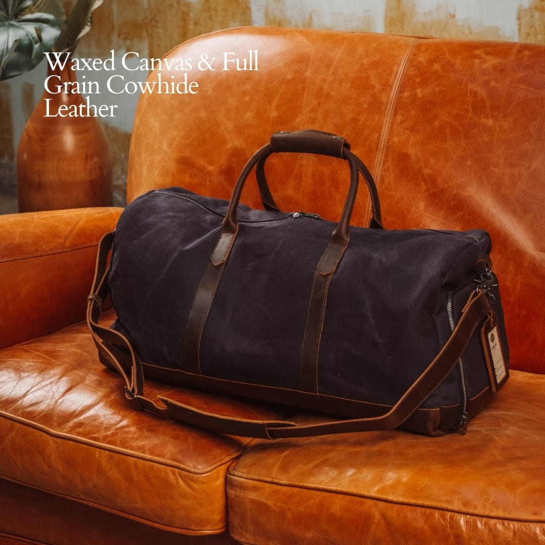 Black waxed canvas duffel bag with leather straps on a brown leather couch.