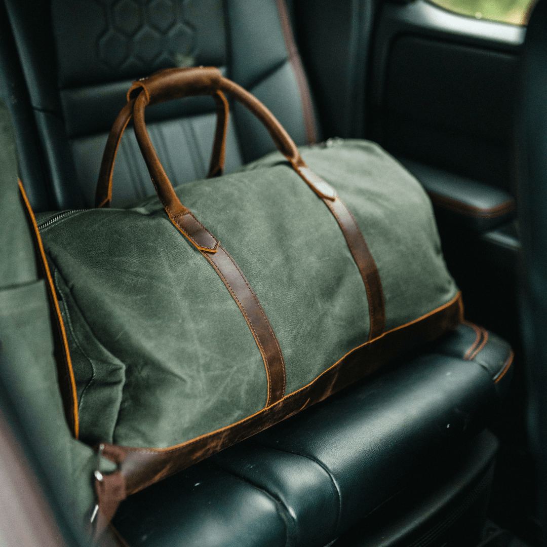 Green duffel bag with brown leather straps on a car seat