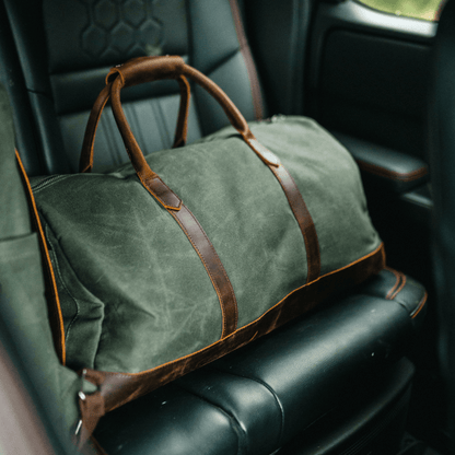 Green duffel bag with brown leather straps on a car seat