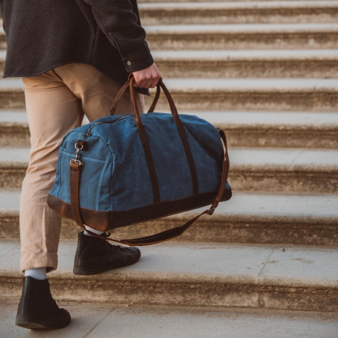 Man holding a blue duffel bag with brown straps on stone steps