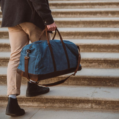 Man holding a blue duffel bag with brown straps on stone steps