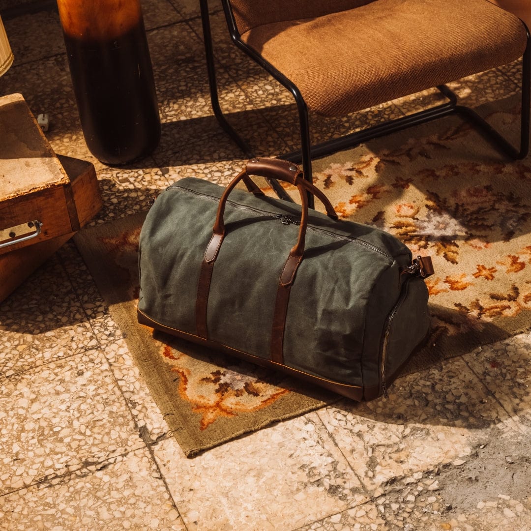 Green duffel bag with brown leather straps on a textured stone floor.