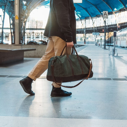 Man walking with a green duffel bag in a train station.