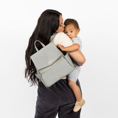 Mom holding a child with Freshly Picked Stone Mini Classic II vegan leather diaper bag backpack with multiple pockets