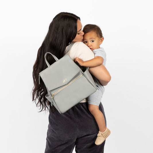 Mom holding a child with Freshly Picked Stone Mini Classic II vegan leather diaper bag backpack with multiple pockets