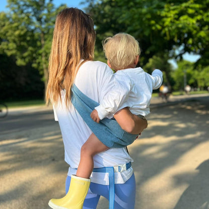 Woman carrying a child in a sling outdoors on a sunny day